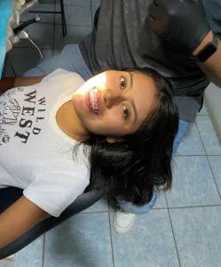 Joven con brackets sonriendo en un consultorio dental tras una revisión de tratamiento de ortodoncia. La imagen destaca la importancia de la higiene bucal y el uso adecuado del cepillo de ortodoncia. Refleja el cuidado en la limpieza dental y la salud dental durante el tratamiento, ideal para quienes buscan información sobre el precio de ortodoncia y el mantenimiento adecuado.