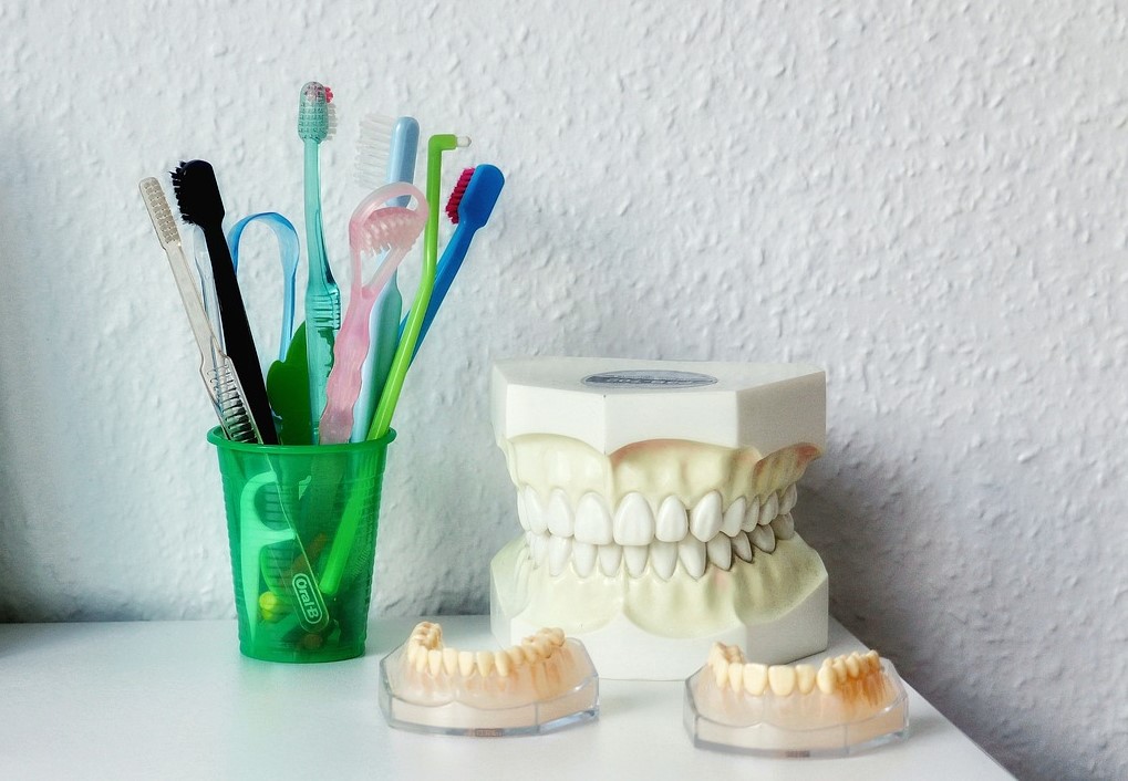 Tipos de cepillos dentales, raspador de lengua, hilo dental y prótesis sobre una superficie, elementos clave para una correcta higiene bucal.