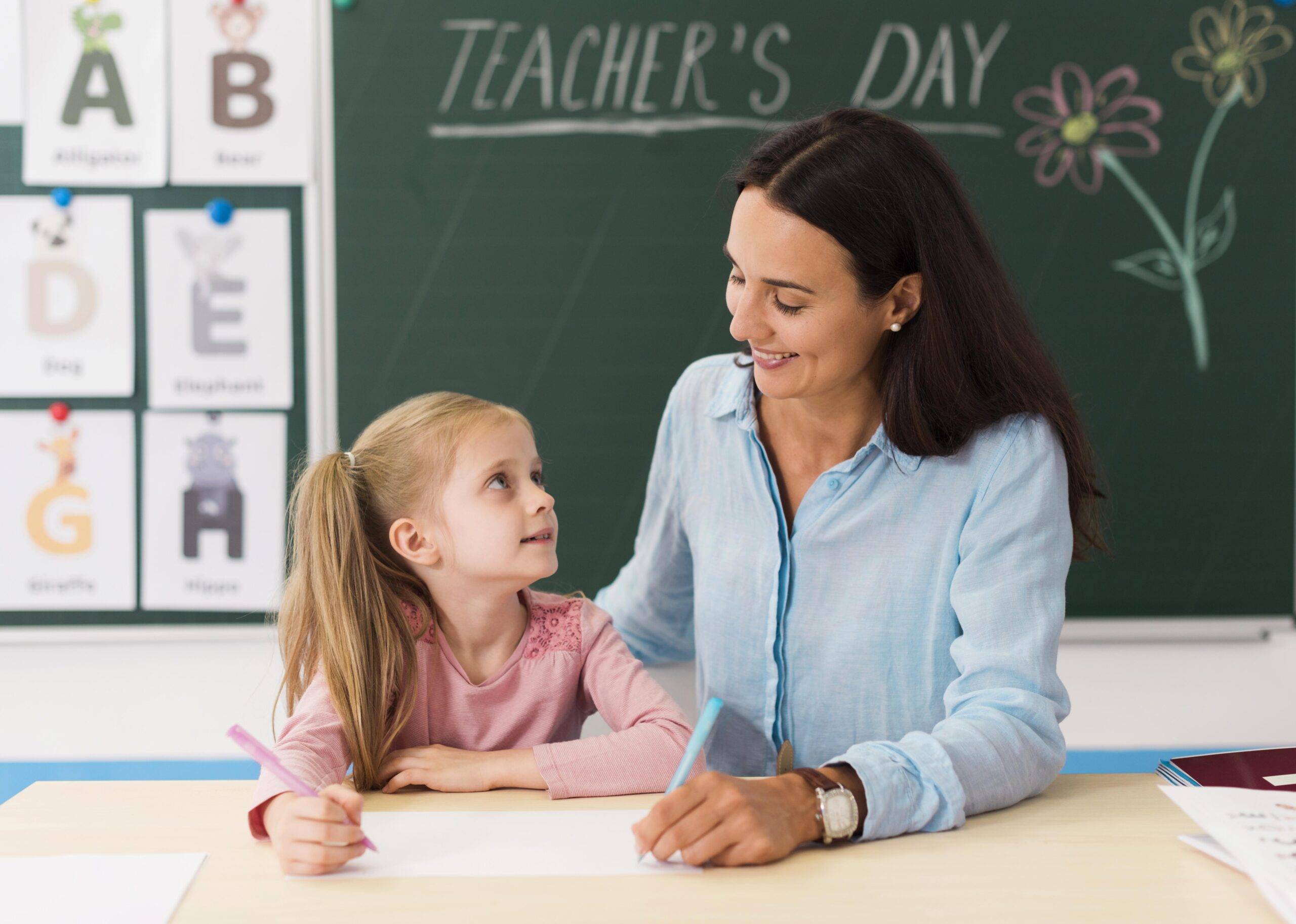 Maestra sonriendo mientras apoya a un alumno en clase, con un ambiente de aprendizaje y afecto.